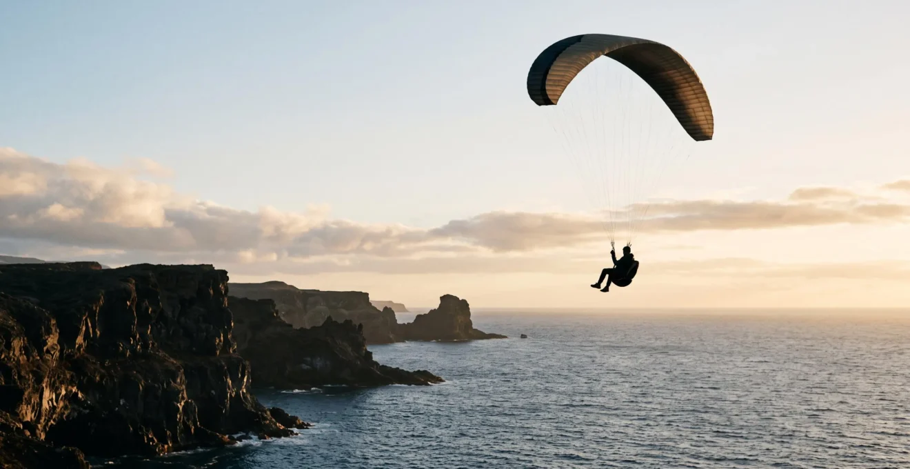 Silhouette d'un parapentiste survolant des falaises volcaniques noires face à l'océan Atlantique aux Canaries au coucher du soleil