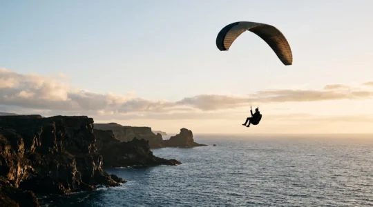 Silhouette d'un parapentiste survolant des falaises volcaniques noires face à l'océan Atlantique aux Canaries au coucher du soleil
