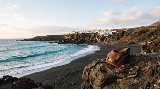 Côte volcanique des Canaries avec plage de sable noir et village blanc en arrière-plan, symbole d'un voyage accessible