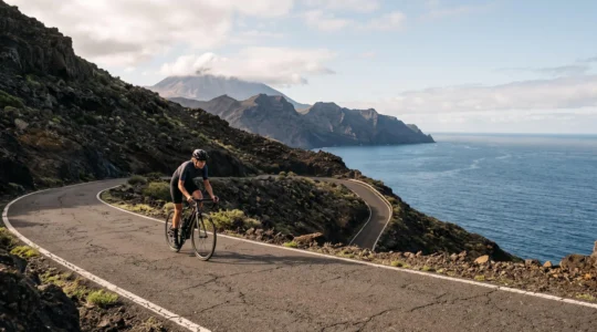 Cycliste solitaire gravissant une route volcanique sinueuse face à l'océan, symbole des activités sportives possibles toute l'année aux Canaries