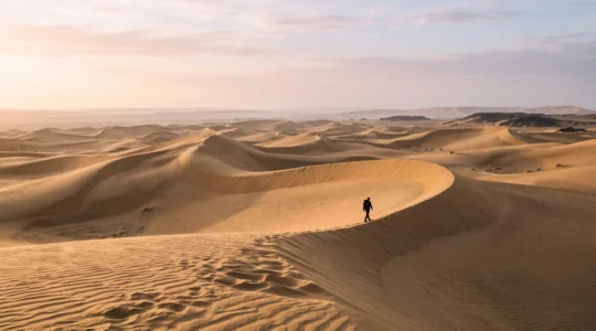 Randonneur solitaire traversant une immense dune dorée aux Canaries au lever du soleil