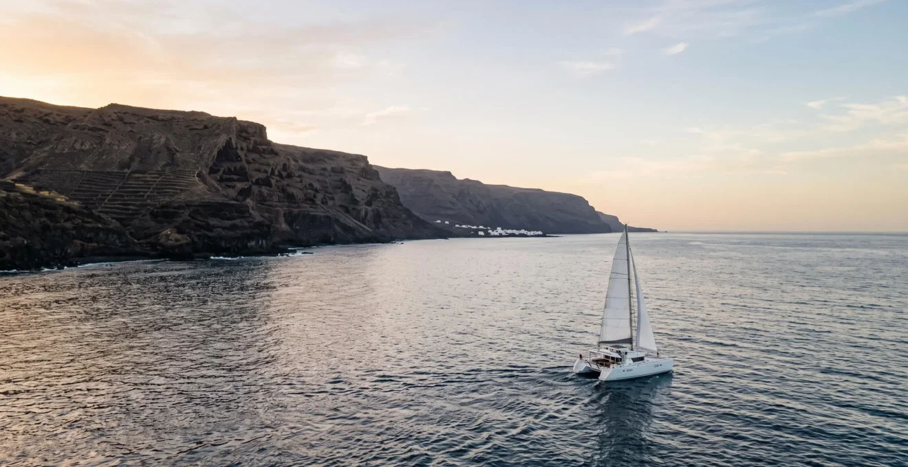 Vue panoramique d'un catamaran voguant au large d'une côte volcanique des Canaries au coucher du soleil