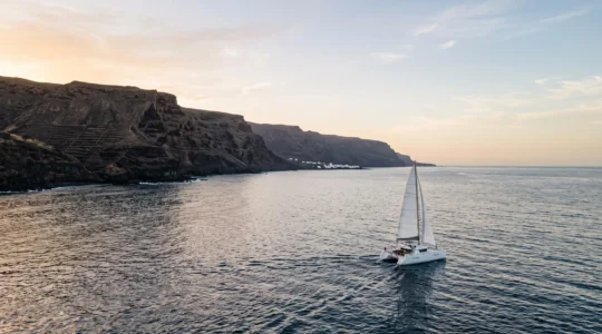 Vue panoramique d'un catamaran voguant au large d'une côte volcanique des Canaries au coucher du soleil
